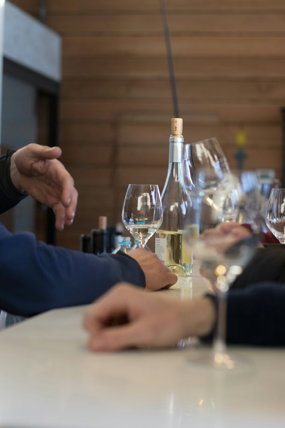 Persone che degustano vino bianco al bancone.