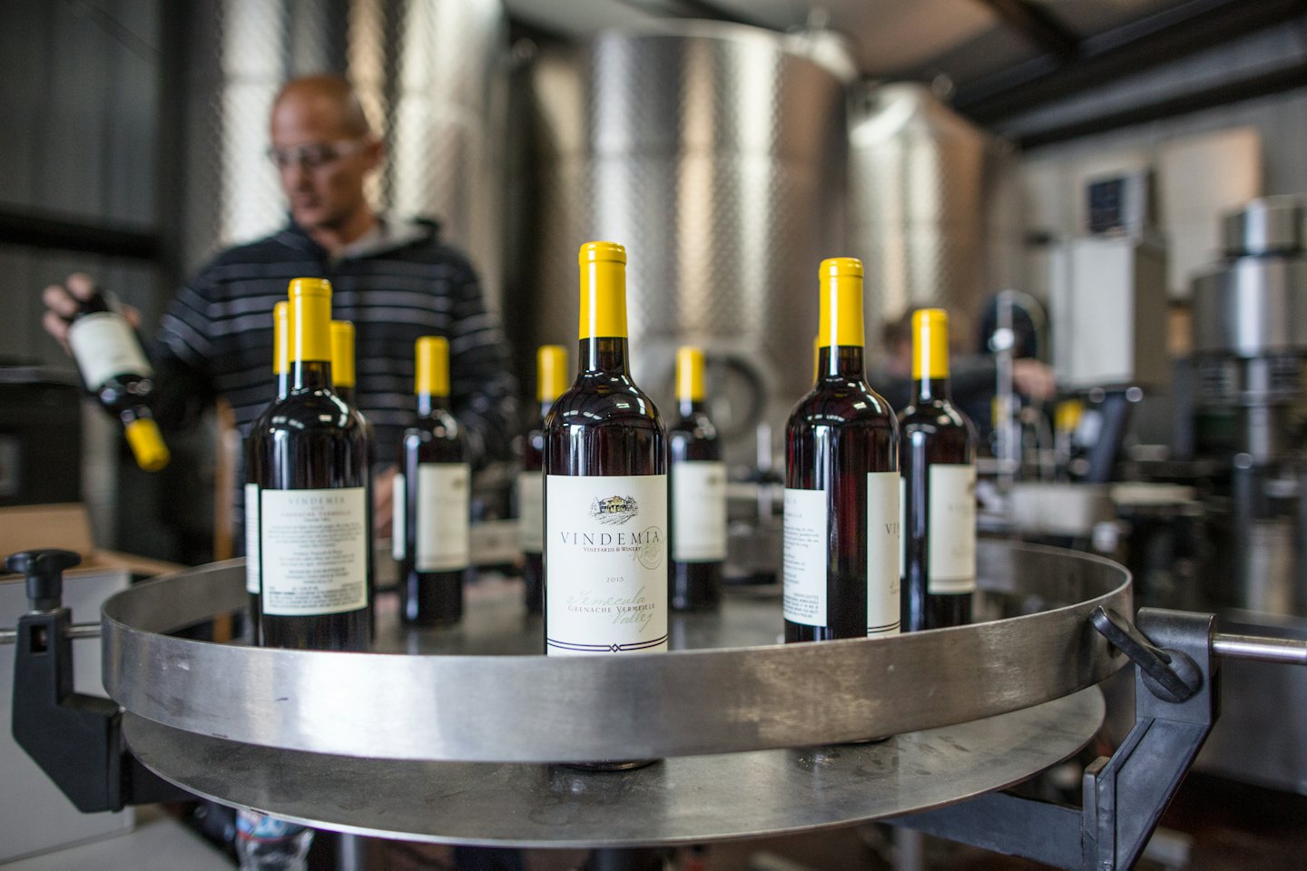 Operaio in una cantina ispeziona bottiglie di vino rosso su un giradischi.