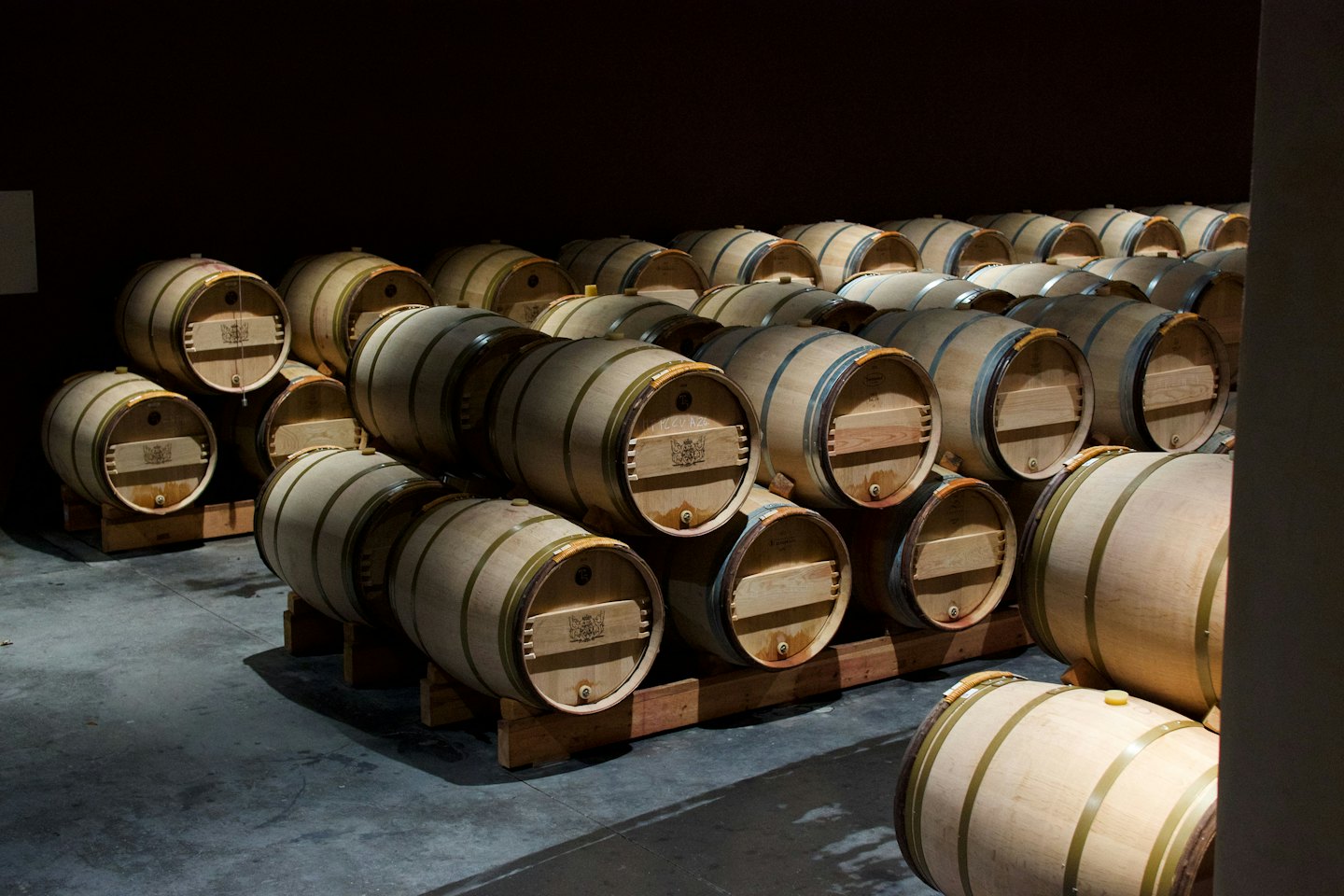 Botti di vino in legno impilate riposano su un pavimento di cantina in cemento.