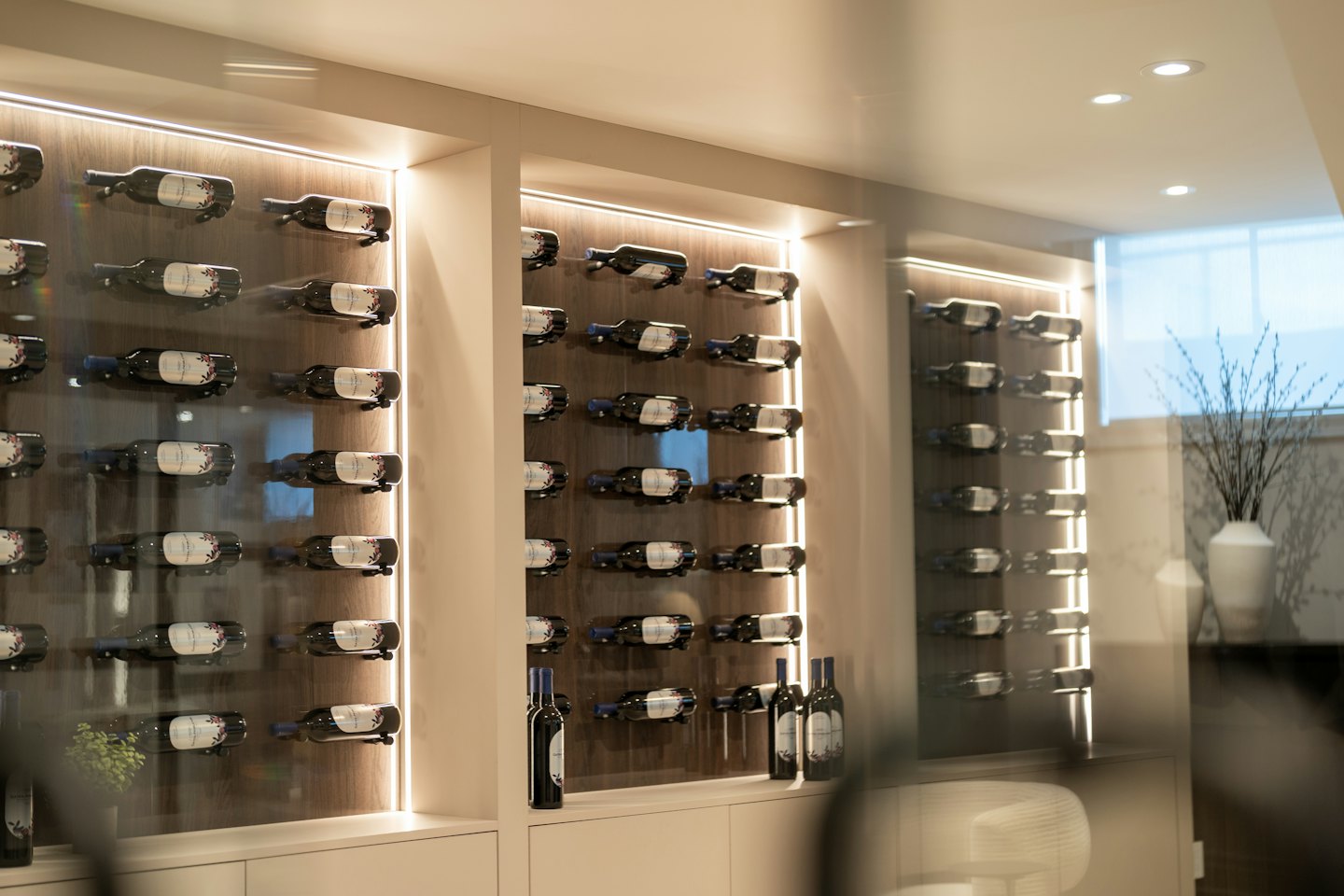 Bottiglie di vino riposano su rastrelliere di legno illuminate all'interno di una cantina di vetro.